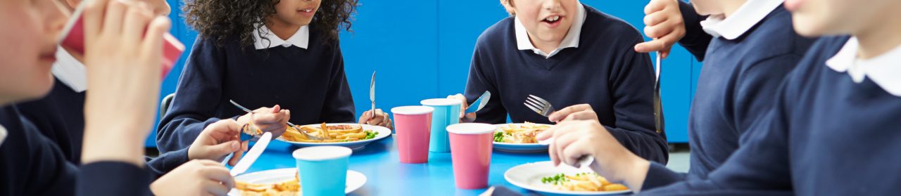 Schoolchildren Sitting At Table Eating Cooked Lunch