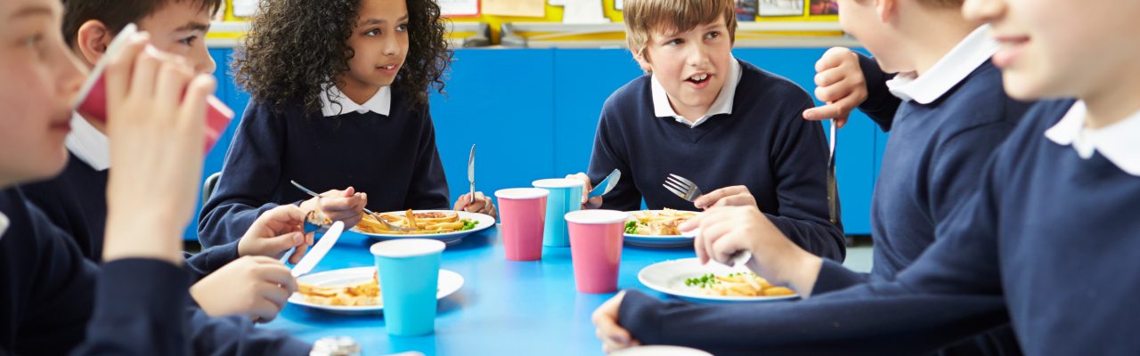 Schoolchildren Sitting At Table Eating Cooked Lunch