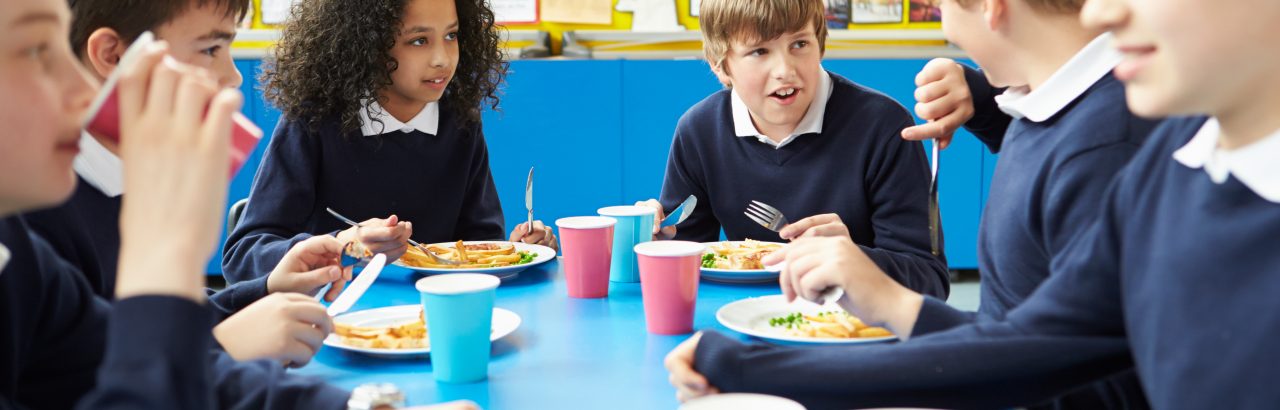 Schoolchildren Sitting At Table Eating Cooked Lunch