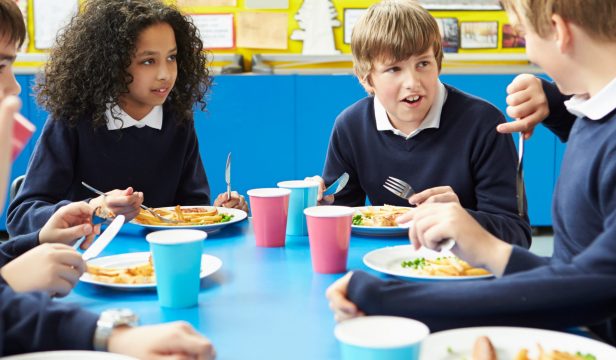 Schoolchildren Sitting At Table Eating Cooked Lunch